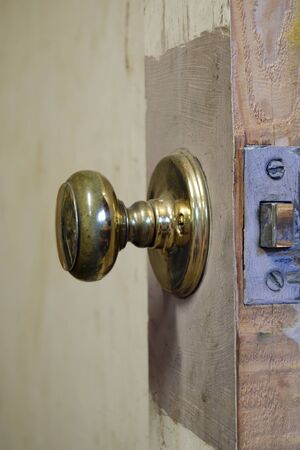 Close view of a brass door knob mounted on a beat up workshop door with an ugly looking finish.の写真素材
