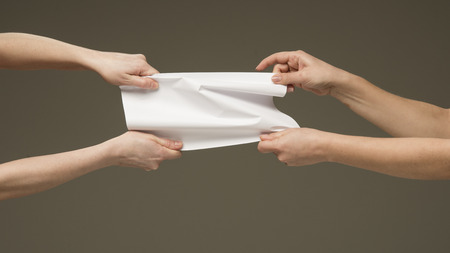 Female hands pulling a white paper in each directionの写真素材