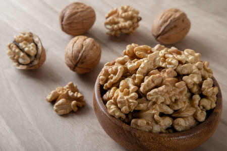 Bowl of walnuts and whole walnut kernels on wooden backgroundの写真素材
