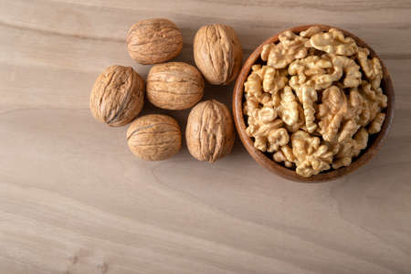 Bowl of walnuts and whole walnut kernels on wooden background,top view