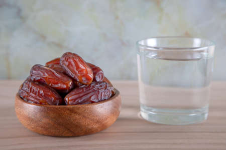 Glass of water with a bowl of date fruit on a wooden background.Muslims break the fast with water...
