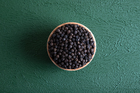 Bowl full of black pepper on a green background