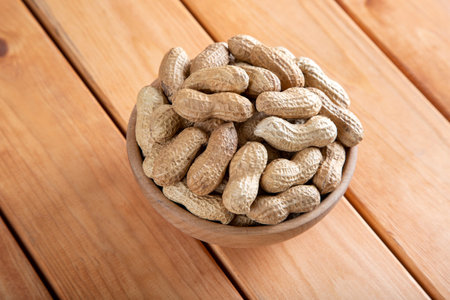 Bowl full of shelled peanuts on wooden background,top view