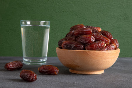 Dried dates in a wooden bowl and a glass of water on a gray background.の写真素材