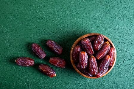 Dates fruit in wooden bowl on green background. Top view.