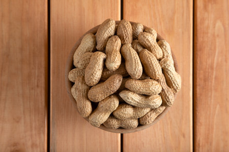 Peanuts in a wooden bowl on a wooden background, top view