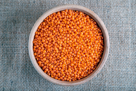 A wooden bowl with red lentil grains on a burlap. Top view of dried orange lentils inside the bowl.の写真素材