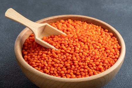 Red lentils in a wooden bowl with a spoon on a black backgroundの写真素材