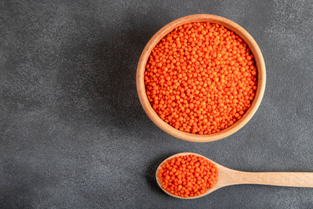 Red lentils in wooden bowl and spoon on dark background, top viewの写真素材