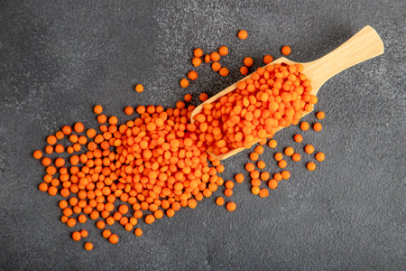 Red lentil grains in a wooden spoon on a gray background. Top view of dried orange lentils in a...