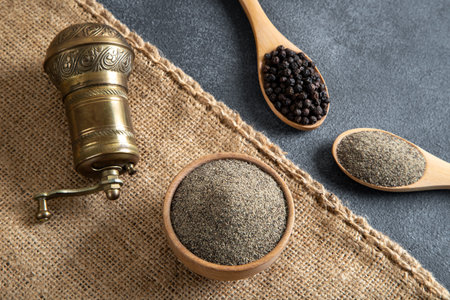 Black pepper in wooden spoon and black pepper mill on sackcloth backgroundの写真素材