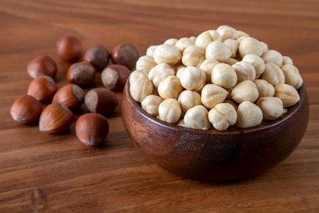 Hazelnut kernels in a wooden bowl with a group of shelled hazelnuts on the tableの写真素材