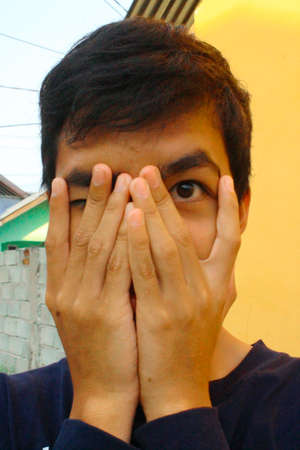 a man covers his face by hand and peeks through a finger.の写真素材