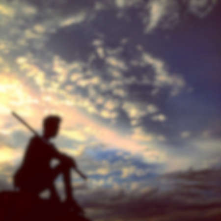 defocused on a silhouette of a man sitting against an orange sky background.