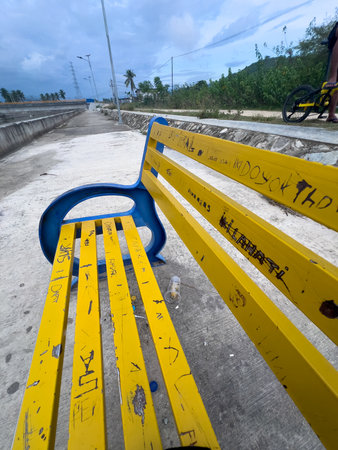 Weathered Blue and Yellow Park Bench with Graffiti and Litter. Vandalismの写真素材