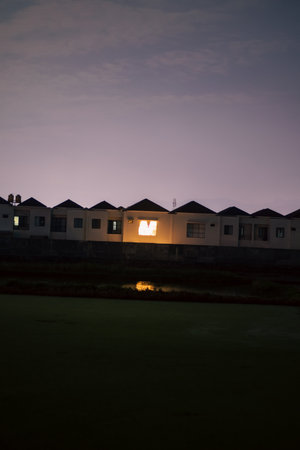 Houses with lights on in the evening with a body of water in the foregroundの写真素材