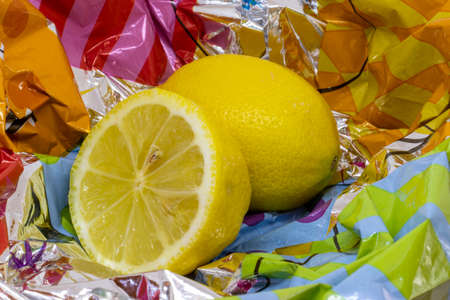Closeup photo of a juicy yellow organic and a half-cut lemon on silver and colorful neon gift wrapping cellophane paperの写真素材