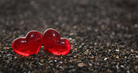 Glass hearts sitting in the colored sands of the seaの写真素材