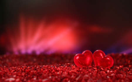 Glass hearts in the sand. In a yellow and orange light background