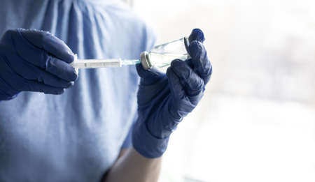 Female hands in blue medical gloves hold a syringe and a bottle of medicine or vaccineの写真素材