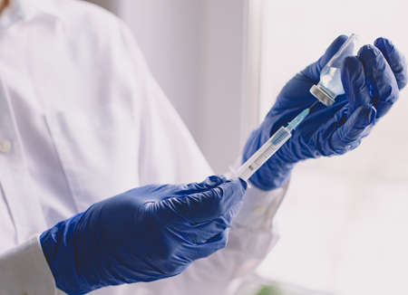 Female hands in blue medical gloves hold a syringe and a bottle of medicine or vaccineの写真素材