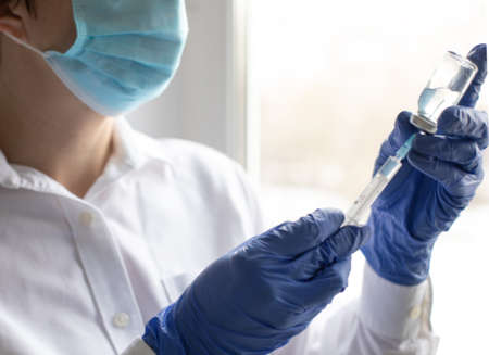 Female hands in blue medical gloves hold a syringe and a bottle of medicine or vaccineの写真素材