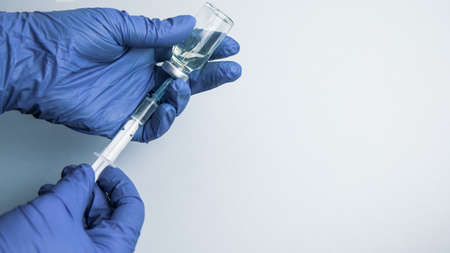 Female hands in blue medical gloves hold a syringe and a bottle of medicine or vaccineの写真素材