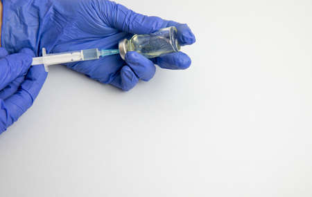 Female hands in blue medical gloves hold a syringe and a bottle of medicine or vaccineの写真素材