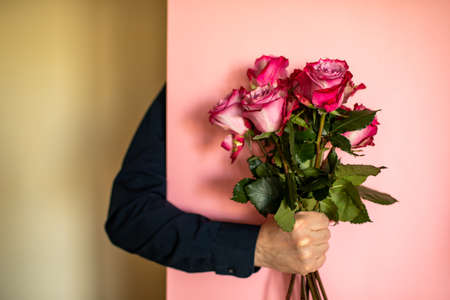 A mans hand in a blue shirt holds a bouquet of roses on a pink background.の写真素材
