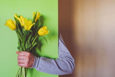 A mans hand holds a bouquet of yellow tulips on a green background. Unexpected surpriseの写真素材