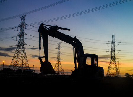 Silhouette of electrical pylon and Backhoe over blue skyの写真素材