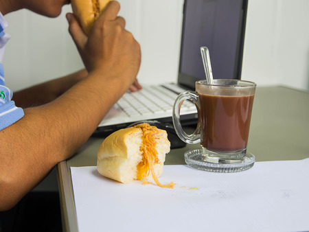 Close up work desk with a computer, bread and cup of coffeeの写真素材