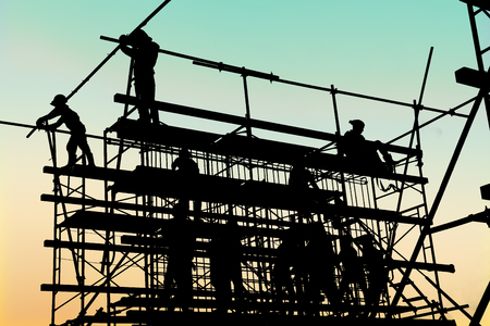 Silhouette of construction workers working on scaffolding at a high level by the standards set must...