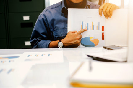 Young businessmen presenting graphs at the quarterly performance report over blurred office. select focus and Film Tone with Light fairの写真素材