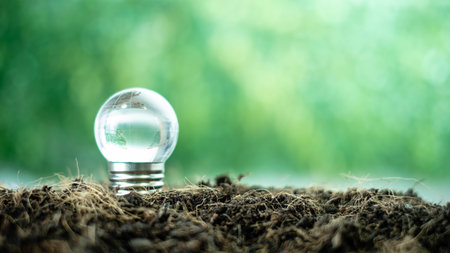 Energy saving light bulb on soil with green bokeh background.の写真素材