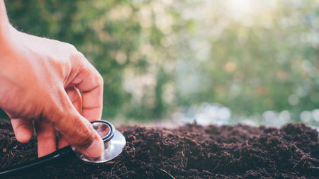 Close up of hand of doctor holding stethoscope and examining soil with green nature background.の写真素材