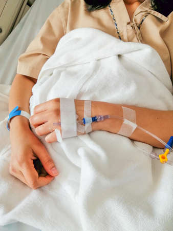 The patient is sleeping on the bed at the hospital with a saline solution line on hand.の写真素材