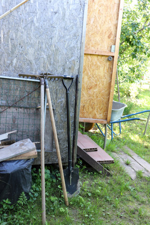 Gardening tools: shovel, hoe, rake near the wall of the shed in the garden. Vertical photo, close-up