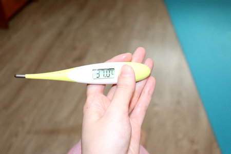 Electronic thermometer in a woman's hand with elevated, subfebrile temperature readings on the...