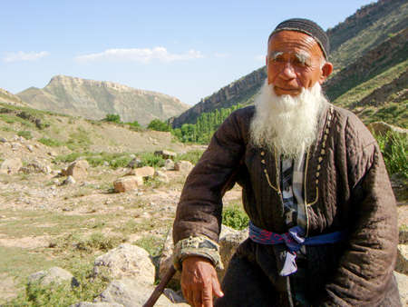 Boysun, Uzbekistan - Jun 8, 2007: The elderly man in traditional Uzbek clothes sitting on a rock in the Boysuntau Mountains.のeditorial素材