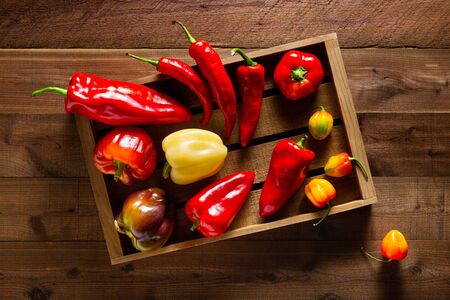 Assortment of peppers in a wood crate on a textured dark wood planks background