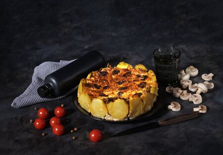 Homemade Lorraine pie with potatoes, chicken, mushrooms, cheese, onions and seasonings. In a black plate, on a dark table, cherry tomatoes, mushrooms, a gray napkin, microgreen and spices. Copy space, horizontal orientationの写真素材