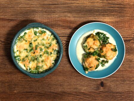 baked cutlets in spinach sauce with cheese on a wooden table in a baking dish and in a plateの写真素材