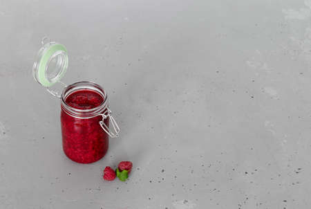 raspberry jam in a glass jar and ripe raspberry berries on a gray concrete backgroundの写真素材