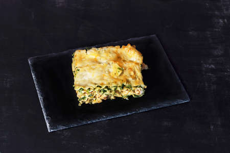 a piece of lasagna on a black background on a slateの写真素材