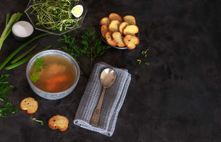 Homemade chicken broth or bouillon with spices, herbs, dill, parsley, onions and microgreens on a black background. Served with crispy crackers, Delicious hot diet food, healthy delicious mealsの写真素材