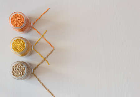 Three glass jars with red, yellow and green lentils on a light background. Nutritious and Important Protein Source. Flat layの写真素材
