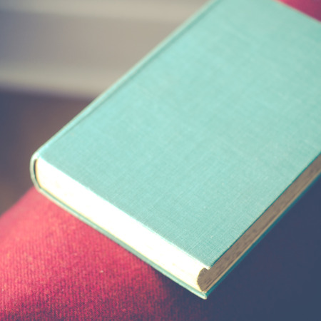 Classic Novel With Blue Cover Resting On Red Wool Blanket On Chairの写真素材