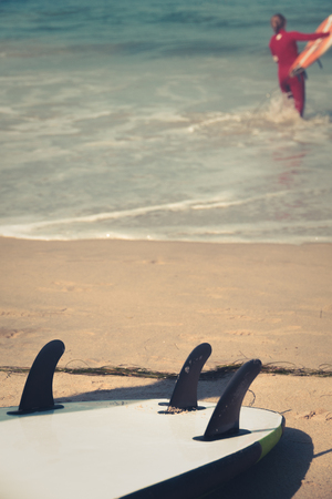 Surfboard on beach with ocean and surfer in backgroundの写真素材