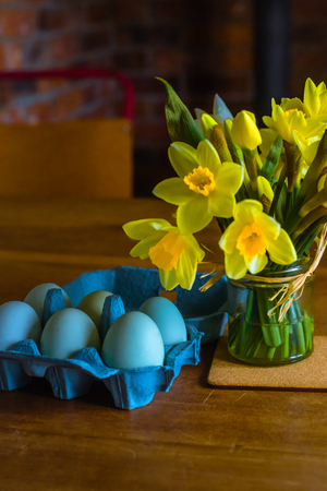 Blue Eggs and Yellow Daffodils on a Wooden Table in Springtimeの写真素材